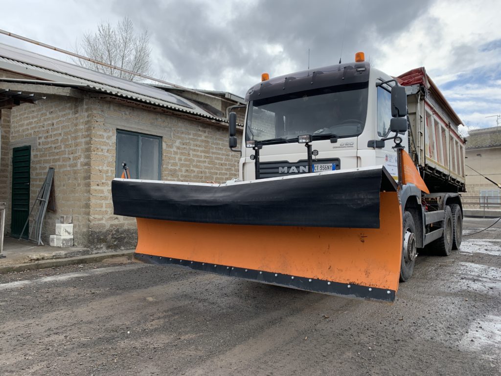 Camion con lama spazzaneve parcheggiato vicino a edificio.