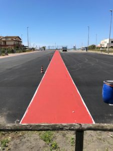 Pista ciclabile rossa su strada asfaltata con coni.