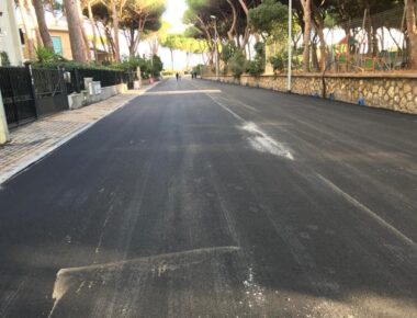 Strada asfaltata con alberi e marciapiedi ai lati.