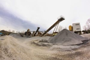 Impianto industriale con nastri trasportatori e cumuli di ghiaia.