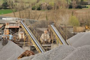 Impianto industriale con nastri trasportatori e cumuli di ghiaia.