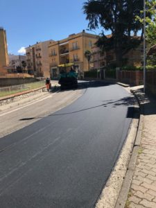 Macchina asfalta strada in quartiere residenziale.