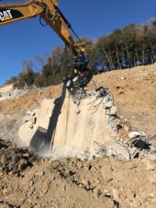 Escavatore demolisce muro di cemento in cantiere.