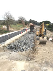 Cantiere stradale con escavatore e camion su strada sterrata.