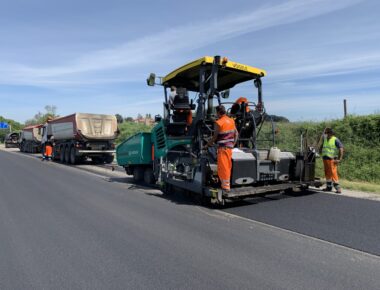 Operai asfaltano una strada con macchinari pesanti.