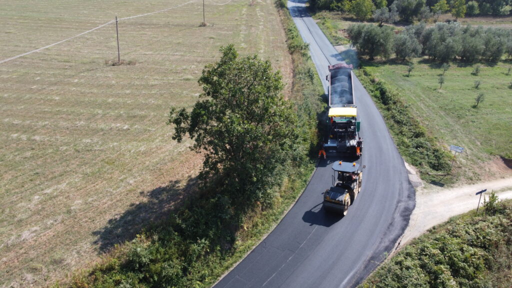 Macchine asfaltano una strada in campagna.