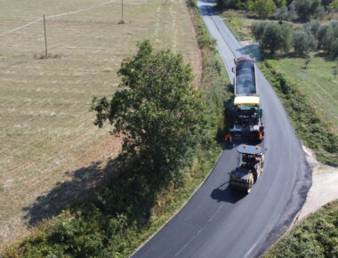 Macchine asfaltano una strada in campagna.