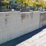 Muro di mattoni chiari in costruzione, alberi sullo sfondo.