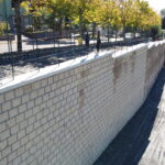 Muro di mattoni con recinzione e cantiere adiacente.