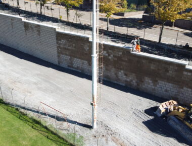 Escavatore vicino a muro di mattoni e operai.