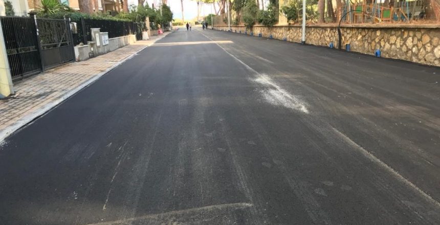 Strada asfaltata con alberi e marciapiedi ai lati.