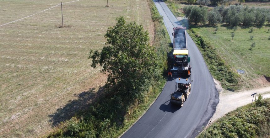 Macchine asfaltano una strada in campagna.