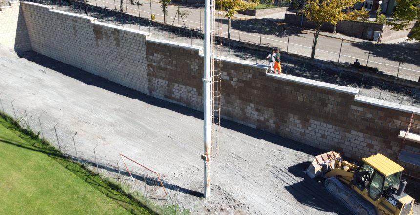 Escavatore vicino a muro di mattoni e operai.