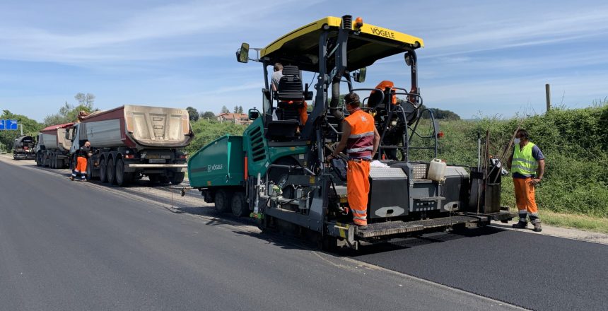 Operai asfaltano una strada con macchinari pesanti.